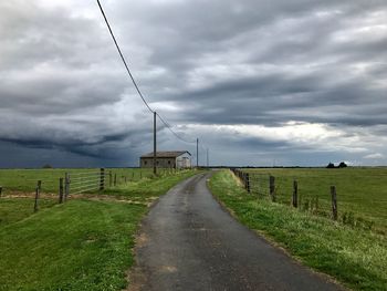 Road amidst field against storm clouds