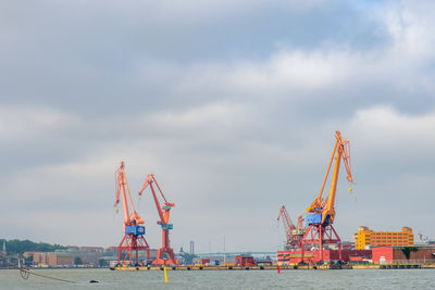 Cranes at commercial dock against sky