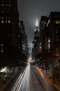 Light trails on city street amidst buildings at night