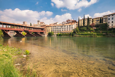 Bridge over river by buildings against sky