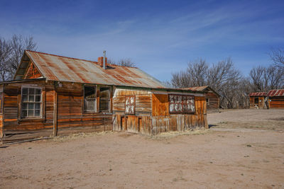 Old wooden house on field by building against sky