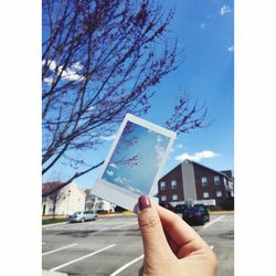 Cropped image of woman hand holding photograph on street against sky