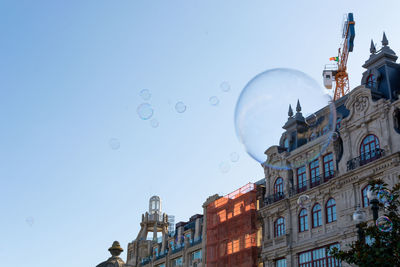 Low angle view of bubbles and buildings against clear sky