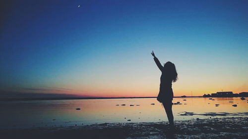 Silhouette woman standing at lakeshore against sky during sunset