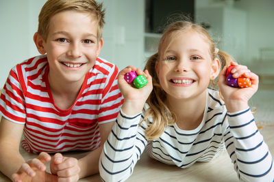 Portrait cheerful siblings playing with dice while lying on carpet at home