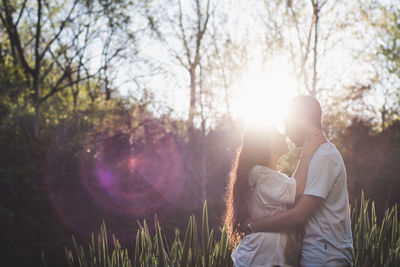 Romantic couple standing against trees during sunny day