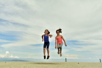 Full length of two girls jumping against the sky