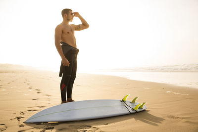 Full length of shirtless man standing on beach against sky