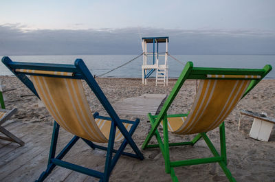 Empty chairs and tables on beach against sky at sunset 