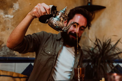 Man pouring drink in glass on table while sitting in restaurant