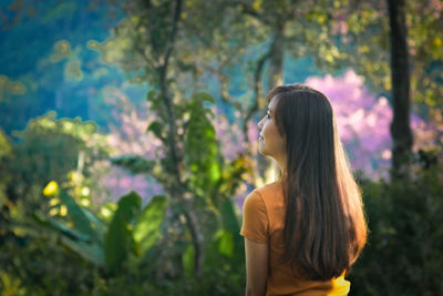 Beautiful woman standing by plants against trees