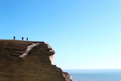 People standing on cliff by sea against clear blue sky