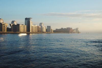 Sea by modern buildings against sky during sunset