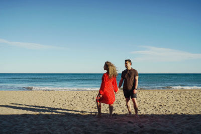 Rear view of woman with man standing at beach against sky