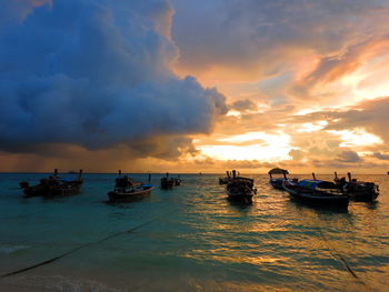 Boats moored in sea against sky during sunset