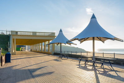 Umbrellas and picnic table by beach against sky on sunny day