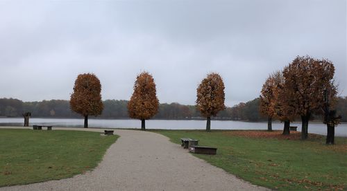 Park bench by autumn trees against sky