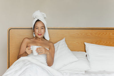 Portrait of young woman sitting on bed at home