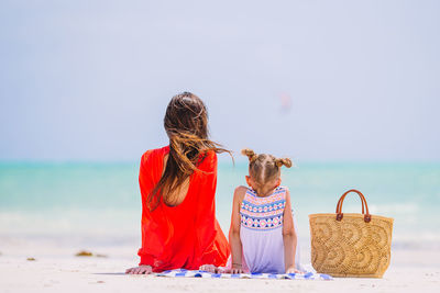 Women sitting on rock by sea against sky