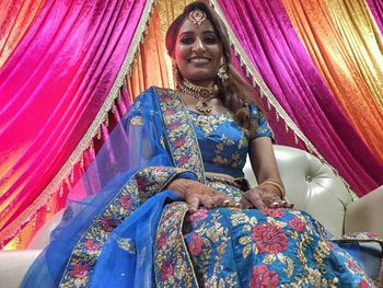 Portrait of smiling bride sitting against curtains