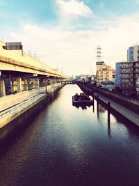 Bridge over river by buildings in city against sky