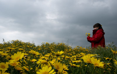 Woman and yellow flowering plants on field against sky