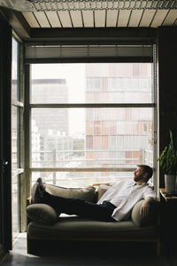 Full length of lonely depressed mature businessman reclining on sofa at office