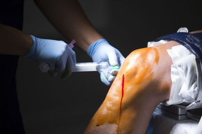 Cropped hands of doctor injecting knee against black background