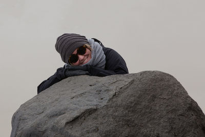 Portrait of smiling mature woman leaning on rock against clear sky