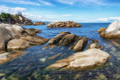 Rocks on shore by sea against sky