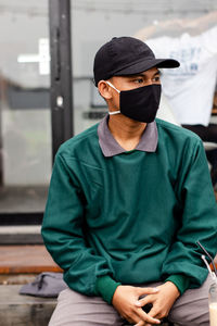 Young man wearing mask sitting outdoors