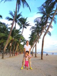 Full length portrait of mother and daughter on beach against sky