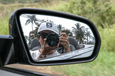 Close-up of mature woman photographing with camera reflecting on side-view mirror