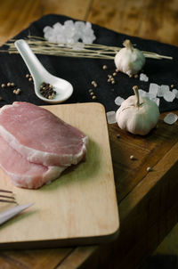 High angle view of salt and meat with garlic on wooden table