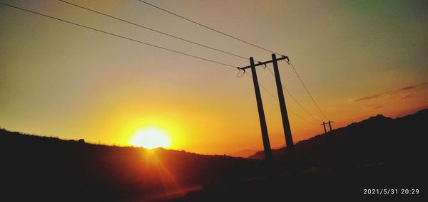 Silhouette electricity pylon against romantic sky at sunset