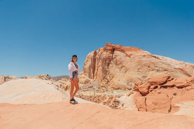 Rear view of woman standing on rock against clear blue sky
