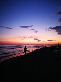 Silhouette man standing on beach against sky during sunset