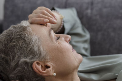 Mature woman lying on couch in living room with closed eyes