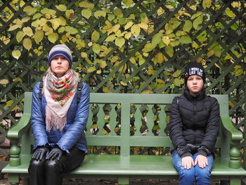 Portrait of mother and daughter sitting on bench against plants