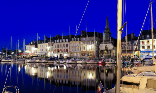 Boats moored at harbor against blue sky in city