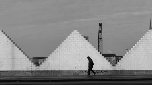 Side view of man walking on footpath against cloudy sky