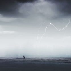 Woman walking on field against storm clouds