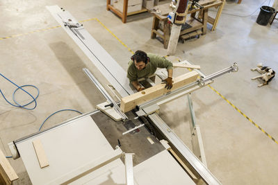 Male carpenter working with wood material at table saw in workshop