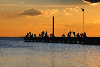 Silhouette people by sea against sky during sunset