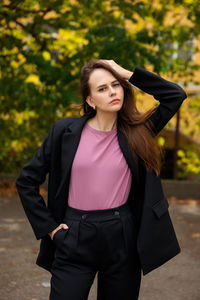 Young woman in black trouser suit and pink t-shirt on the background of the park