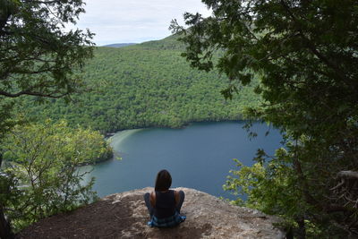 Rear view of woman sitting on rock by lake against sky