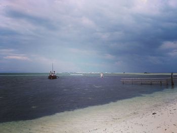 Boats sailing in calm sea against cloudy sky