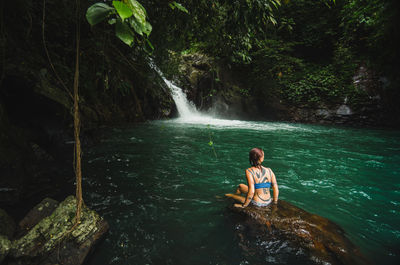 Woman sitting on rock against waterfall in forest