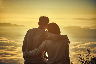 Rear view of man embracing woman while looking at view during sunset