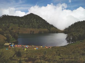Tents on land by lake against cloudy sky